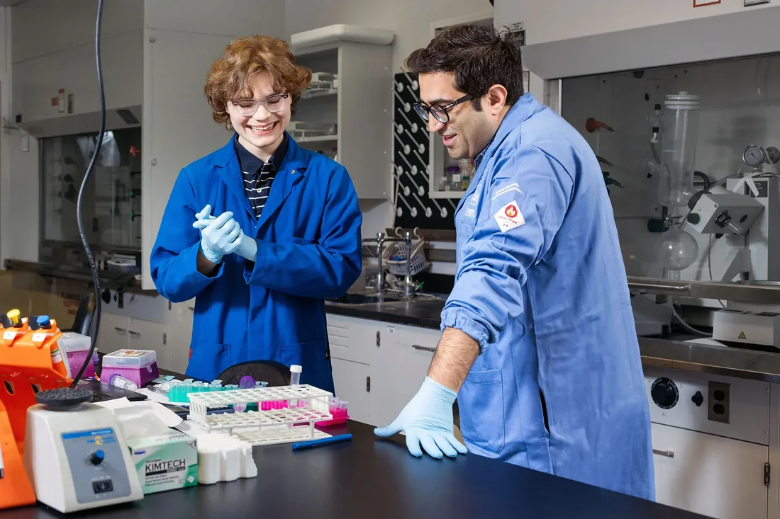 an undergraduate student and professor look at samples on a lab bench while wearing PPE