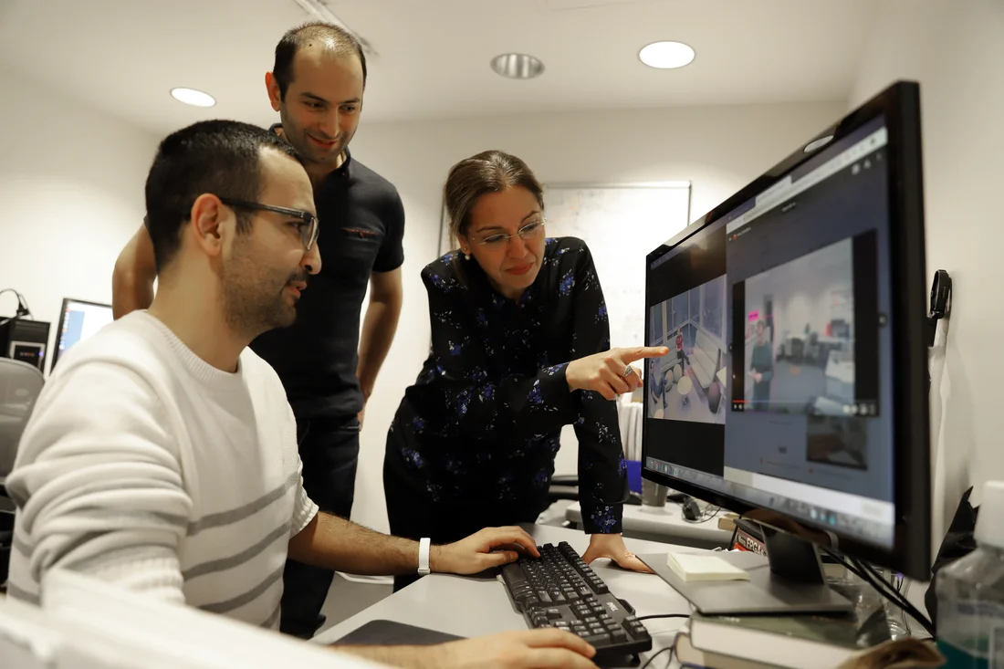 Students working on a laptop and a professor pointing at the laptop screen