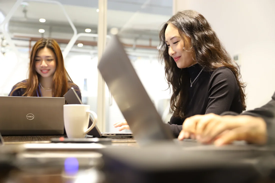 Two smiling students work on laptops