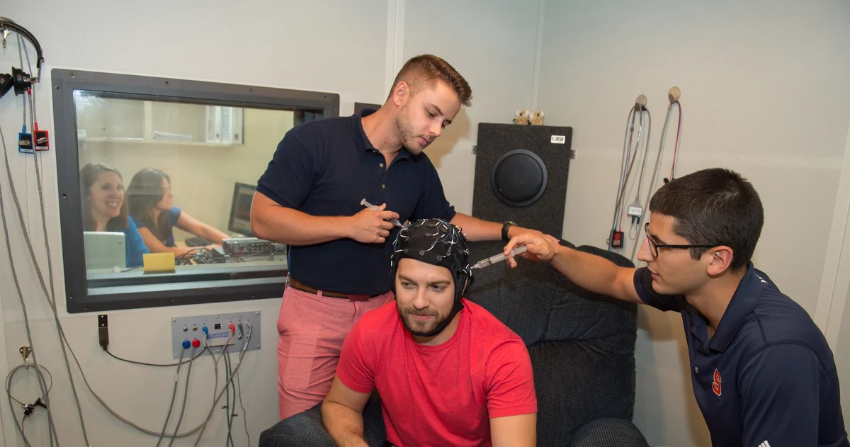 Two students work with a patient, who is wearing an EEG cap.