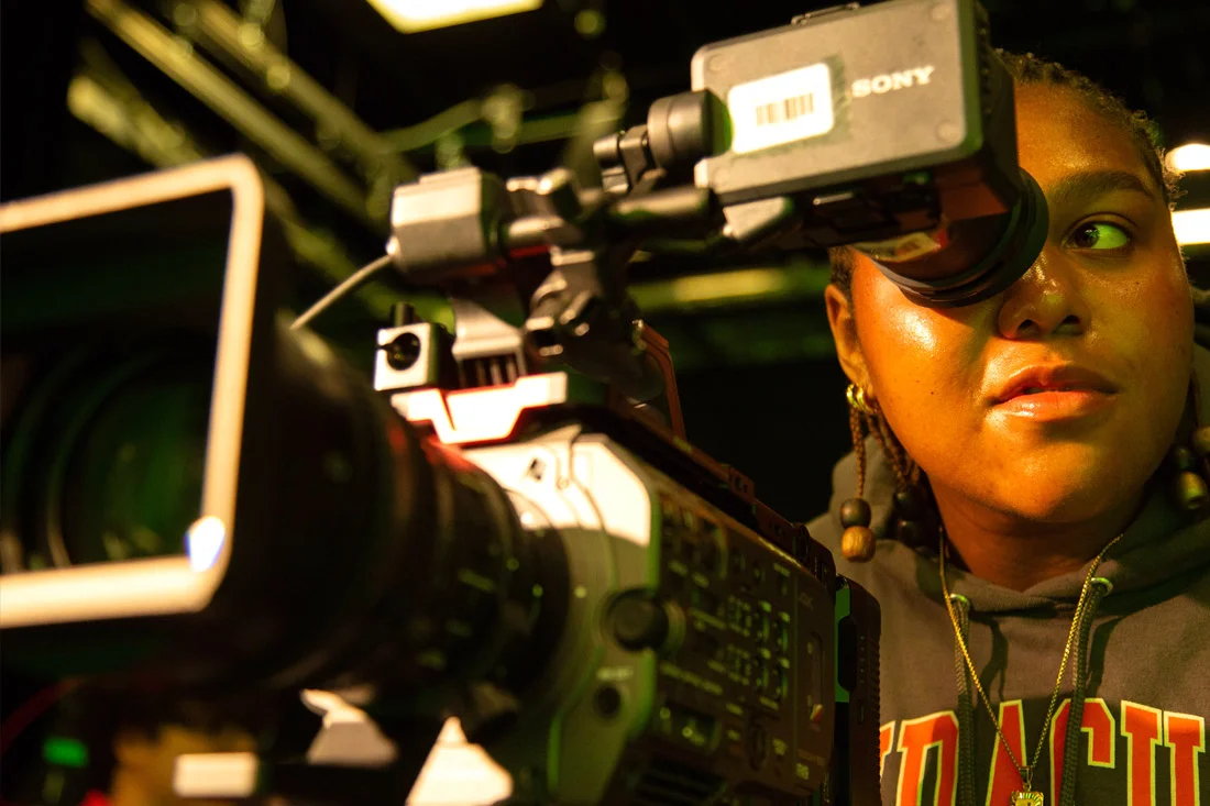 A student behind a camera in a green screen studio, shown in close-up.