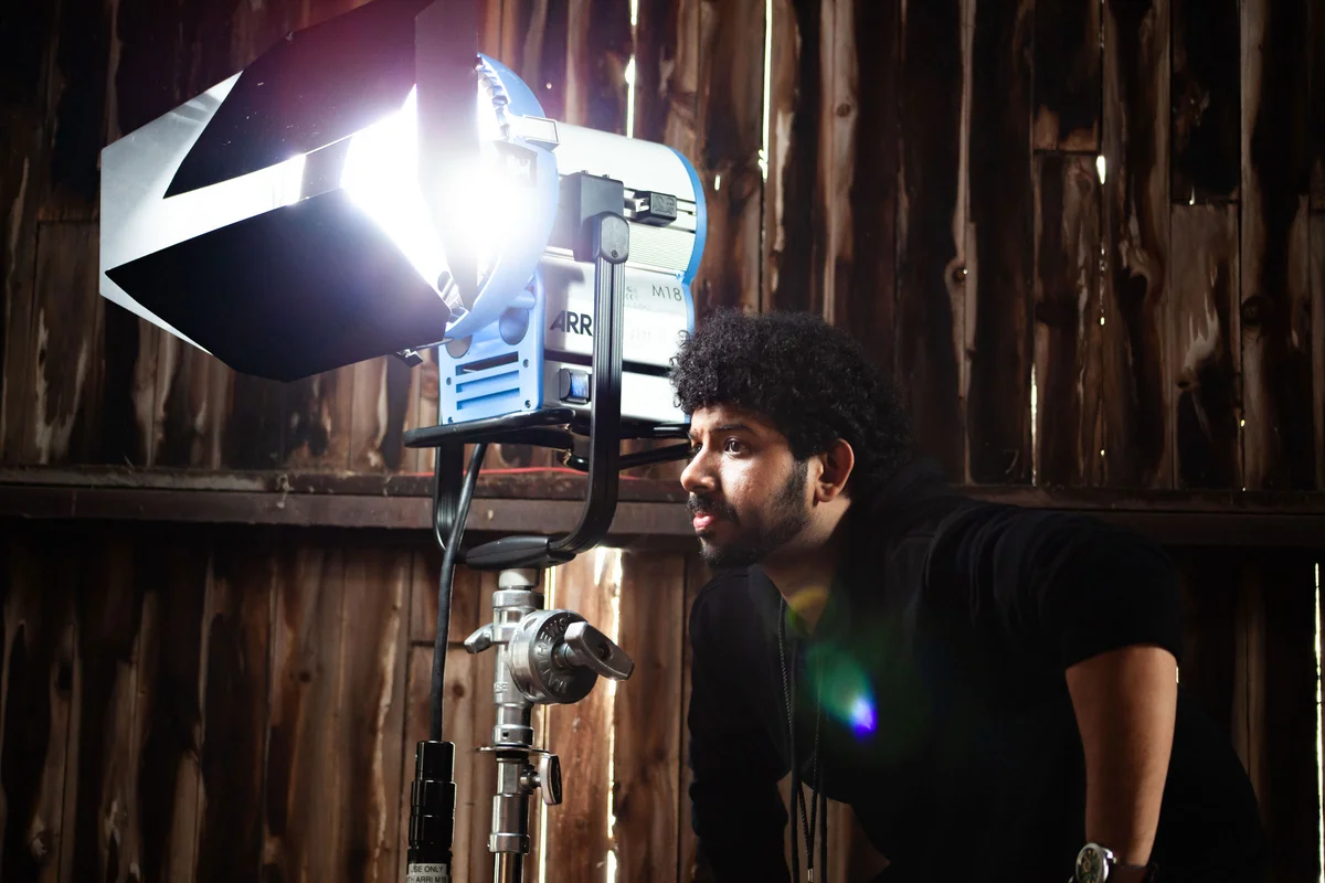 A person stands next to a large light on a film set.