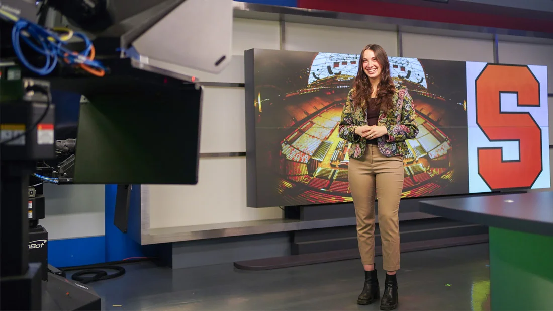 Student reporting in front of a camera inside the Dick Clark Studio.