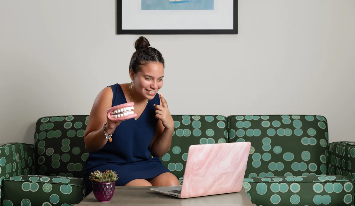 A student smiles and holds a dental model up to a laptop while on a video call.