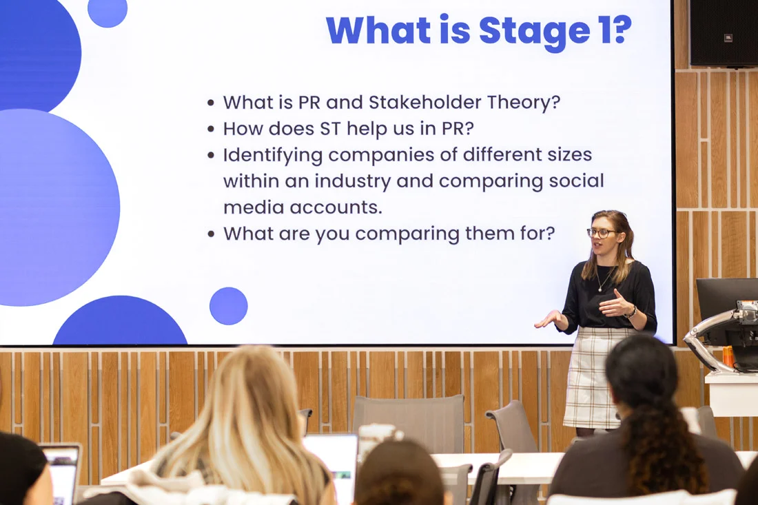 Students watch a professor give a presentation in a large lecture hall.