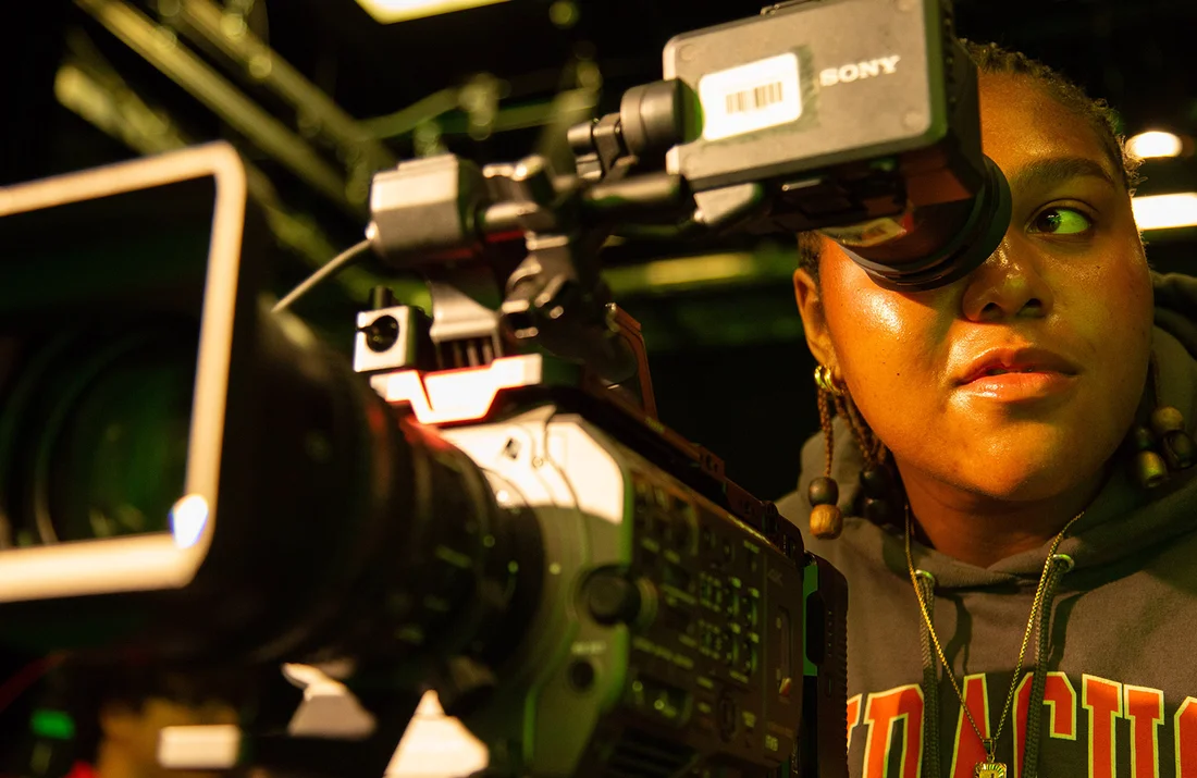 A student using camera equipment in a green screen studio.