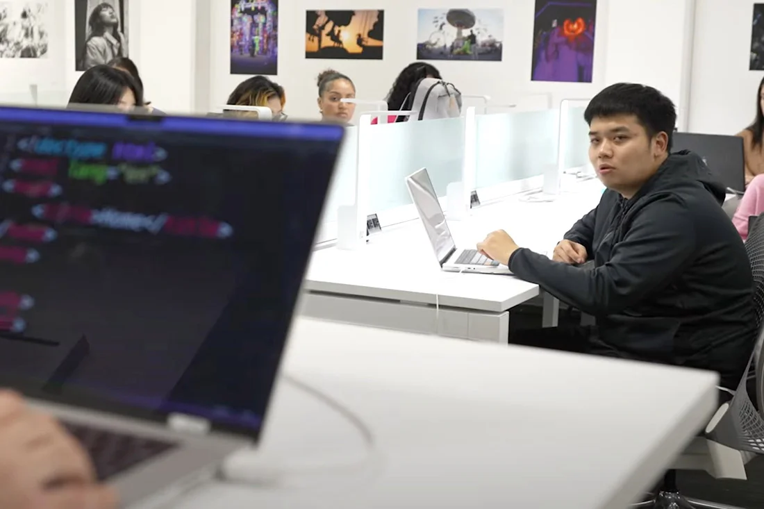 Student looking up at a professor giving a presentation about code.