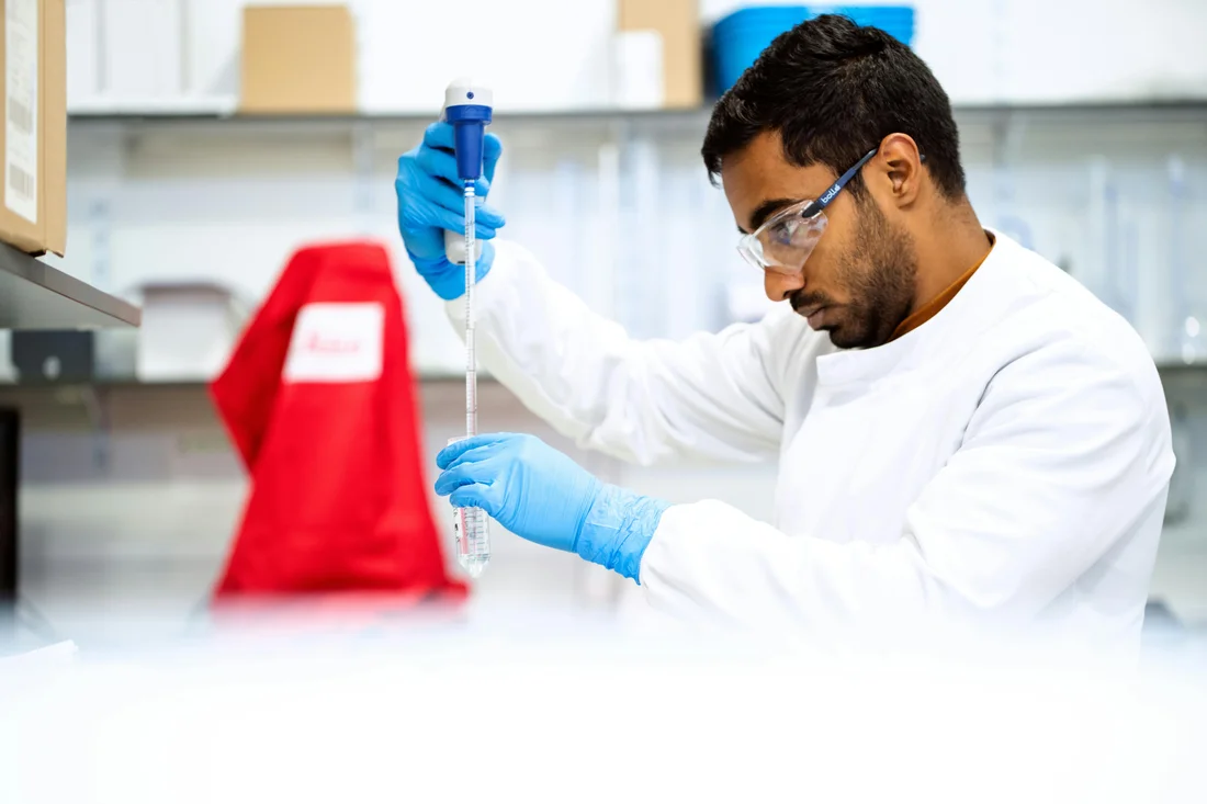 a person wearing PPE pulls up a sample using a glass pipetter