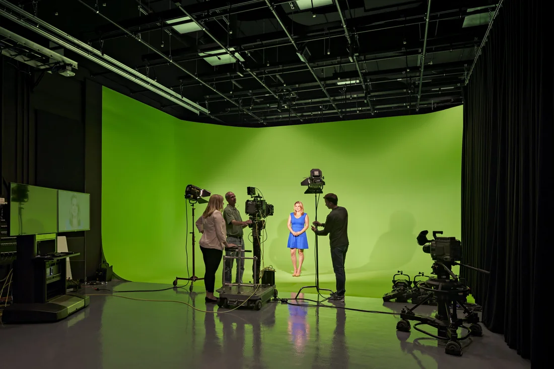 Students and an instructor in the television, radio and film program working together on set in front of a green screen.