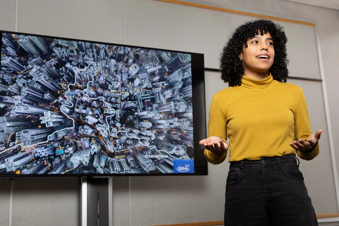 A student stands in front of a large screen while giving a presentation.