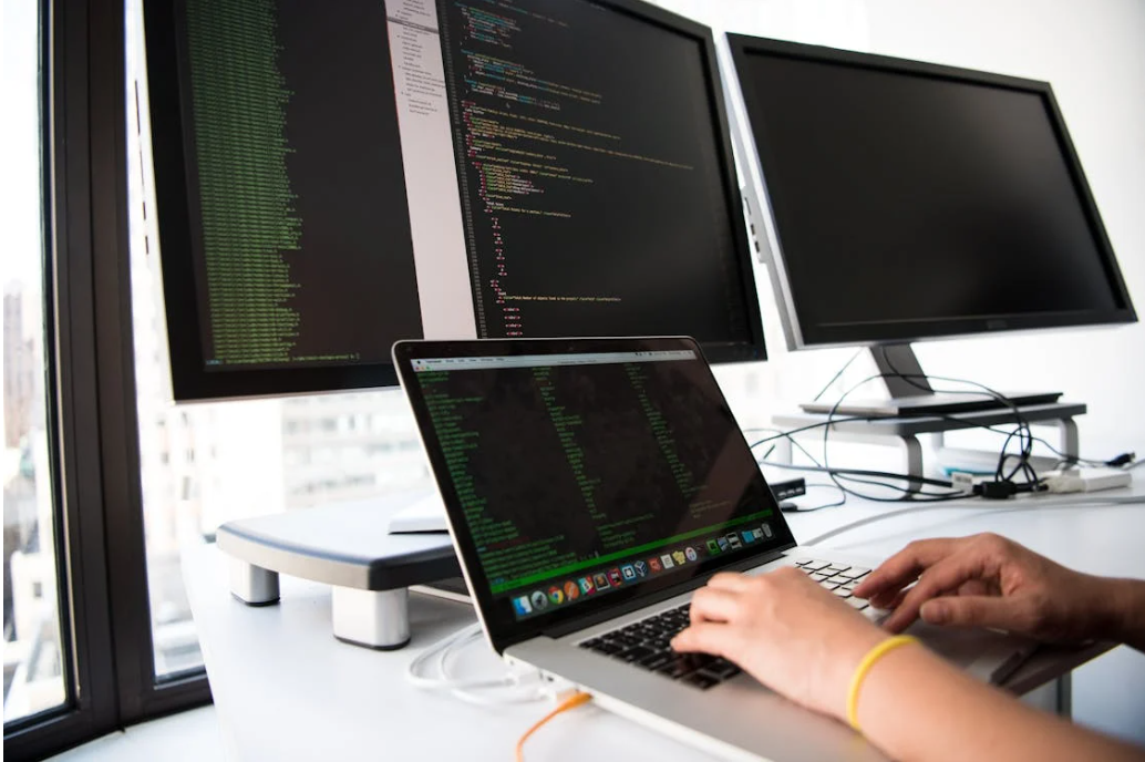 A person types on a computer. Additional monitors show lines of code.